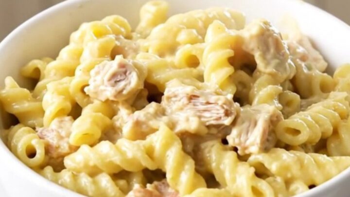 A white bowl filled with creamy chicken pot pie pasta, showing chunks of chicken and colorful vegetables in a thick sauce.