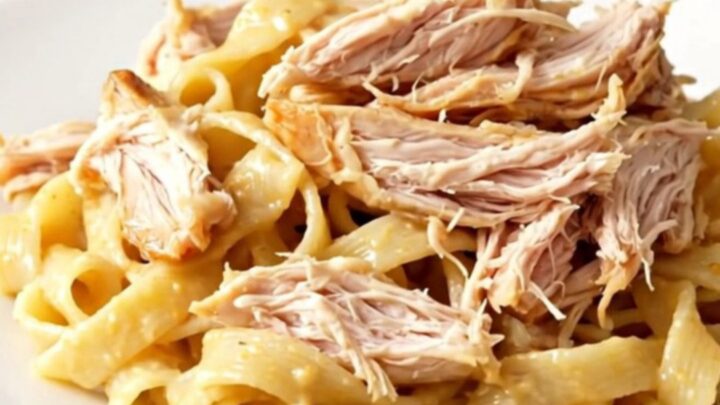 A close-up of creamy shredded chicken with sun-dried tomatoes in a slow cooker.
