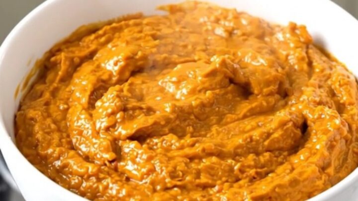 A white bowl filled with creamy, shredded buffalo chicken dip, steaming and glossy.