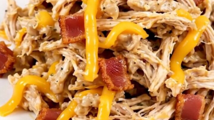 A close-up of shredded jalapeno popper chicken served on a white plate with visible bits of melted cheese and jalapenos.