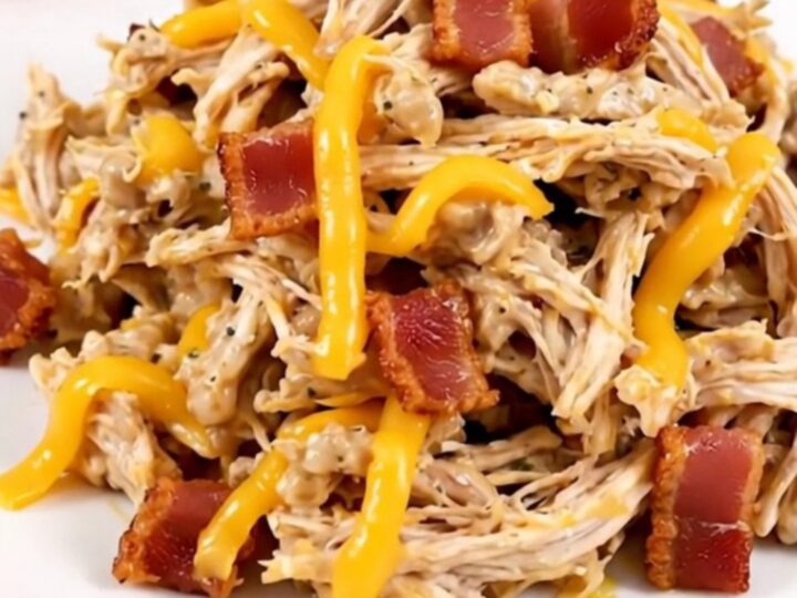 A close-up of shredded jalapeno popper chicken served on a white plate with visible bits of melted cheese and jalapenos.