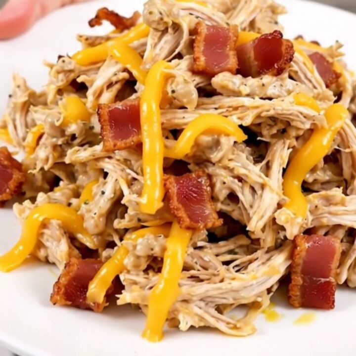 A close-up of shredded jalapeno popper chicken served on a white plate with visible bits of melted cheese and jalapenos.