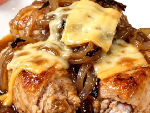 A close-up of tender chicken breasts topped with melted Swiss cheese and caramelized onions in a slow cooker.
