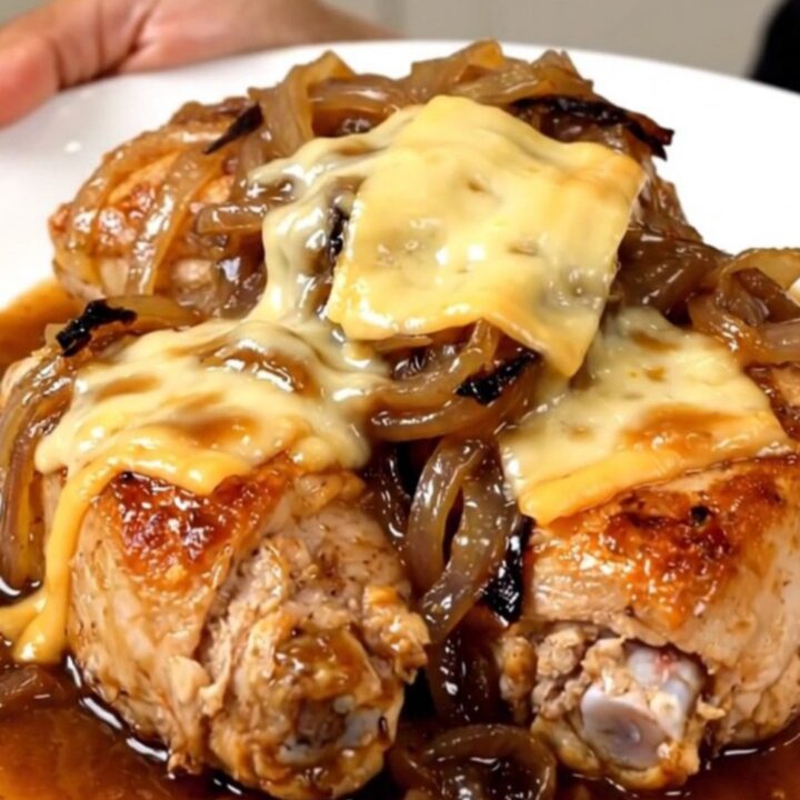 A close-up of tender chicken breasts topped with melted Swiss cheese and caramelized onions in a slow cooker.