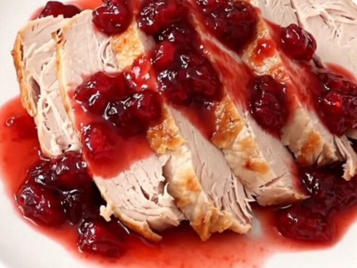 A sliced turkey breast on a white plate, drizzled with a glossy, red cranberry orange glaze.