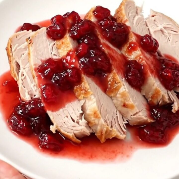 A sliced turkey breast on a white plate, drizzled with a glossy, red cranberry orange glaze.