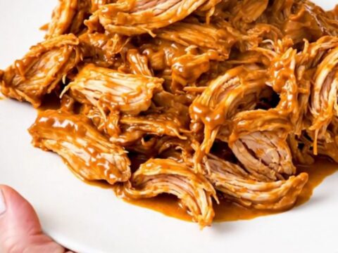 A slow cooker filled with creamy salsa chicken, black beans, and melted cream cheese on a white speckled countertop.