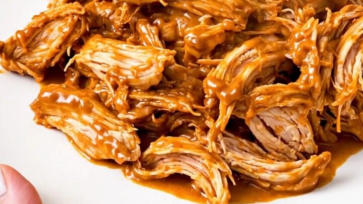 A slow cooker filled with creamy salsa chicken, black beans, and melted cream cheese on a white speckled countertop.