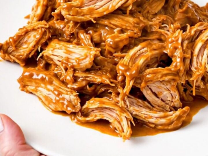 A slow cooker filled with creamy salsa chicken, black beans, and melted cream cheese on a white speckled countertop.