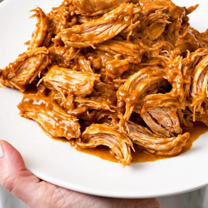 A slow cooker filled with creamy salsa chicken, black beans, and melted cream cheese on a white speckled countertop.