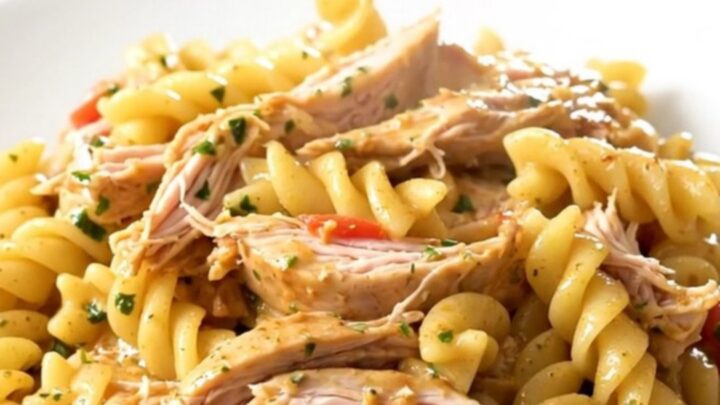 A top-down view of a slow cooker filled with chicken, cherry tomatoes, and a wheel of garlic herb cheese.