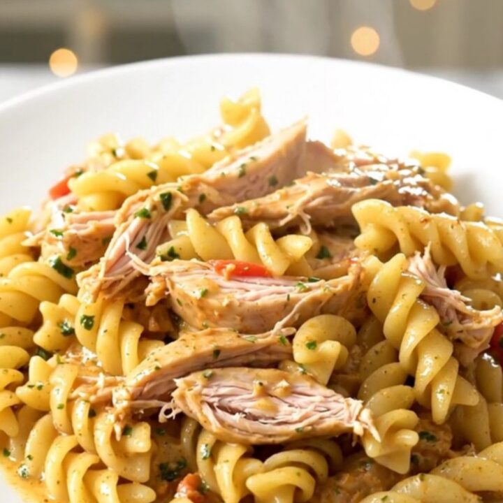 A top-down view of a slow cooker filled with chicken, cherry tomatoes, and a wheel of garlic herb cheese.