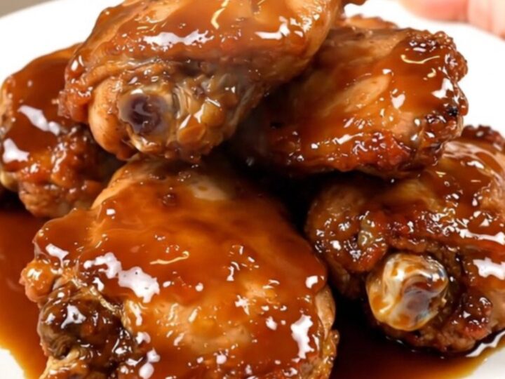 A close-up shot of glossy, honey garlic glazed chicken thighs on a white plate.
