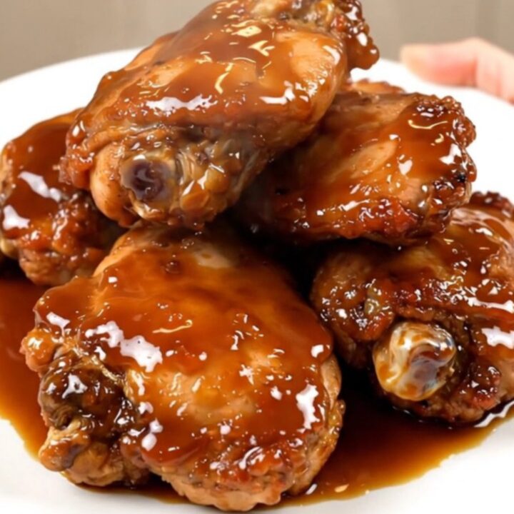 A close-up shot of glossy, honey garlic glazed chicken thighs on a white plate.
