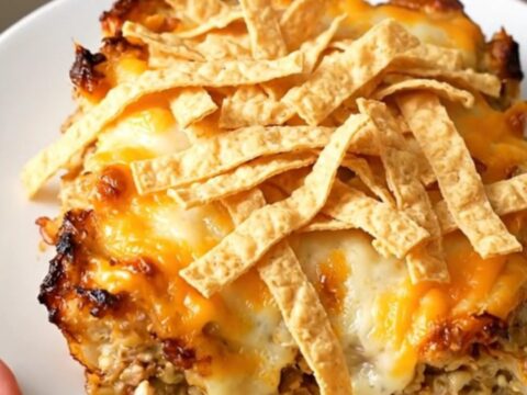 A steaming, creamy slow cooker chicken enchilada casserole served on a white plate with melted cheese and crispy tortilla