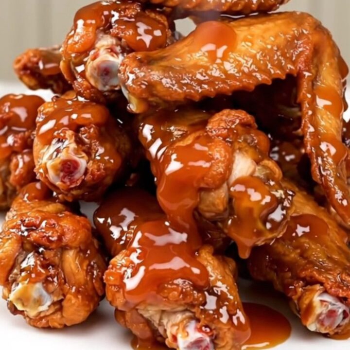 A bowl of glossy, caramelized sweet chili chicken wings served on a white plate.
