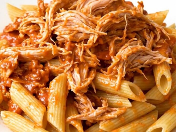 A top-down view of creamy tomato basil chicken served over penne pasta on a white plate.