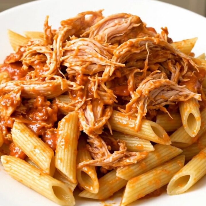 A top-down view of creamy tomato basil chicken served over penne pasta on a white plate.