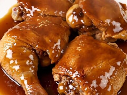 A close-up view of tender, glazed chicken thighs resting on a white plate with a glossy maple-dijon finish.