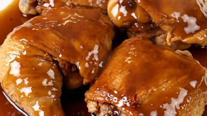 A close-up view of tender, glazed chicken thighs resting on a white plate with a glossy maple-dijon finish.