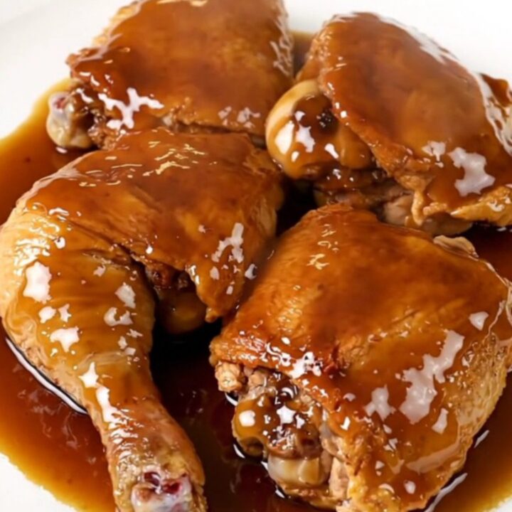 A close-up view of tender, glazed chicken thighs resting on a white plate with a glossy maple-dijon finish.
