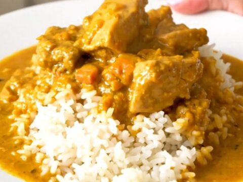 A close-up of creamy pumpkin curry chicken served over white rice in a bowl.