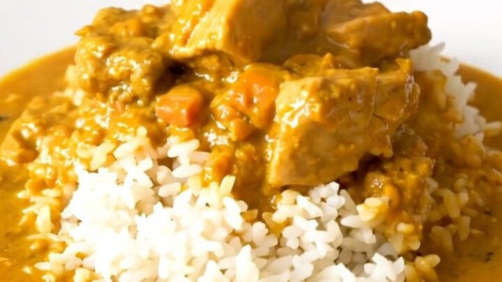 A close-up of creamy pumpkin curry chicken served over white rice in a bowl.