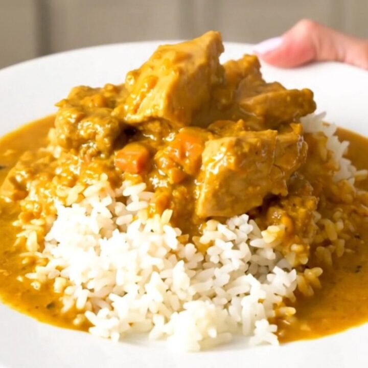 A close-up of creamy pumpkin curry chicken served over white rice in a bowl.