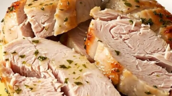 A close-up of sliced, succulent turkey tenderloin medallions glistening with warm lemon herb juices on a white plate.