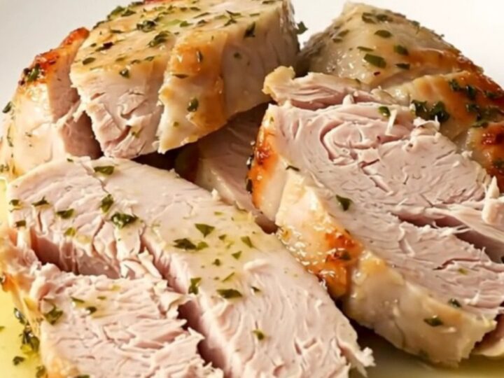 A close-up of sliced, succulent turkey tenderloin medallions glistening with warm lemon herb juices on a white plate.