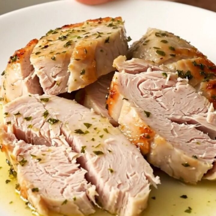A close-up of sliced, succulent turkey tenderloin medallions glistening with warm lemon herb juices on a white plate.