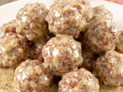 A top-down view of a black slow cooker filled with turkey meatballs, bacon, ranch seasoning, and cubes of cream cheese.