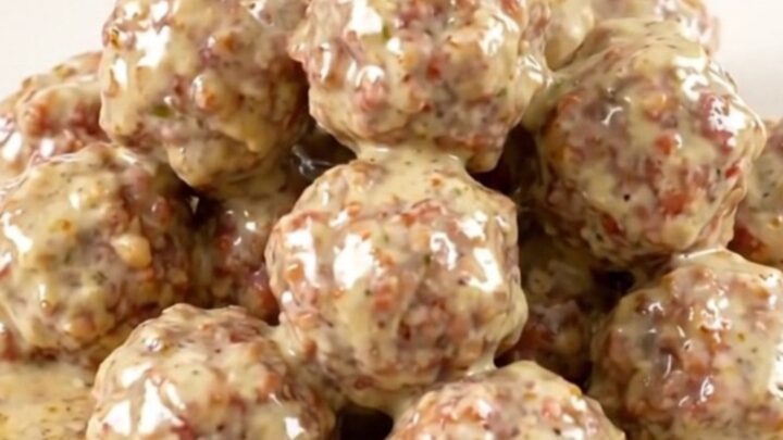 A top-down view of a black slow cooker filled with turkey meatballs, bacon, ranch seasoning, and cubes of cream cheese.