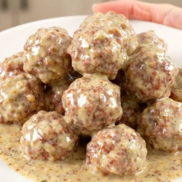 A top-down view of a black slow cooker filled with turkey meatballs, bacon, ranch seasoning, and cubes of cream cheese.