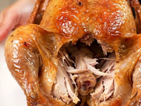 A golden-brown slow cooker whole chicken on a white plate, steaming and ready to be carved.