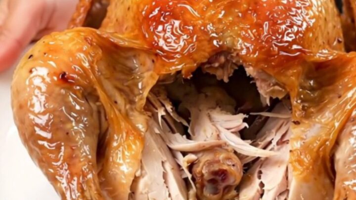 A golden-brown slow cooker whole chicken on a white plate, steaming and ready to be carved.