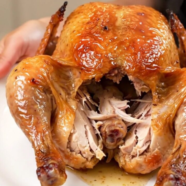 A golden-brown slow cooker whole chicken on a white plate, steaming and ready to be carved.
