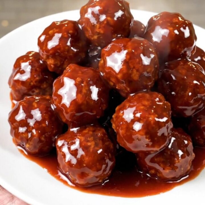 A close-up view of steaming, glossy meatballs covered in a thick, dark red glaze in a slow cooker.