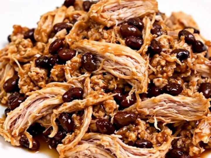 A top-down view of a slow cooker filled with raw chicken, black beans, seasoning, and salsa.
