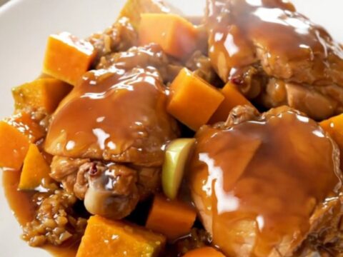 A close-up of tender chicken thighs with roasted butternut squash and apple wedges on a white plate.