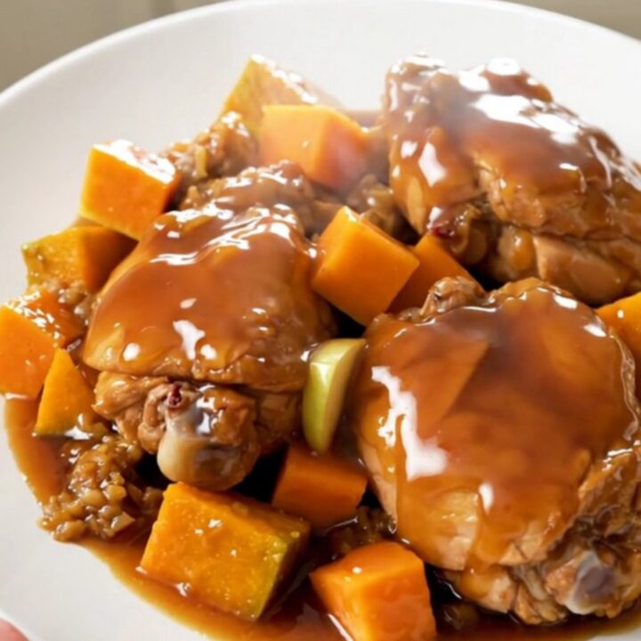 A close-up of tender chicken thighs with roasted butternut squash and apple wedges on a white plate.