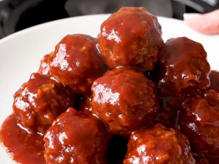A top-down view of a black slow cooker filled with meatballs covered in a glossy cranberry chili sauce.