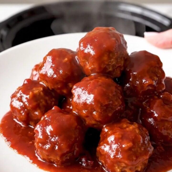 A top-down view of a black slow cooker filled with meatballs covered in a glossy cranberry chili sauce.