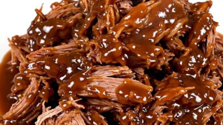 A close-up of tender, shredded apple cider pulled pork served on a white plate.