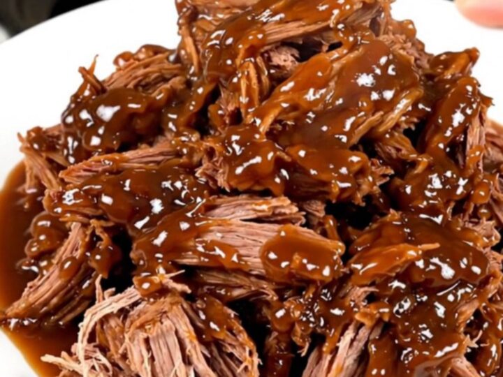 A close-up of tender, shredded apple cider pulled pork served on a white plate.