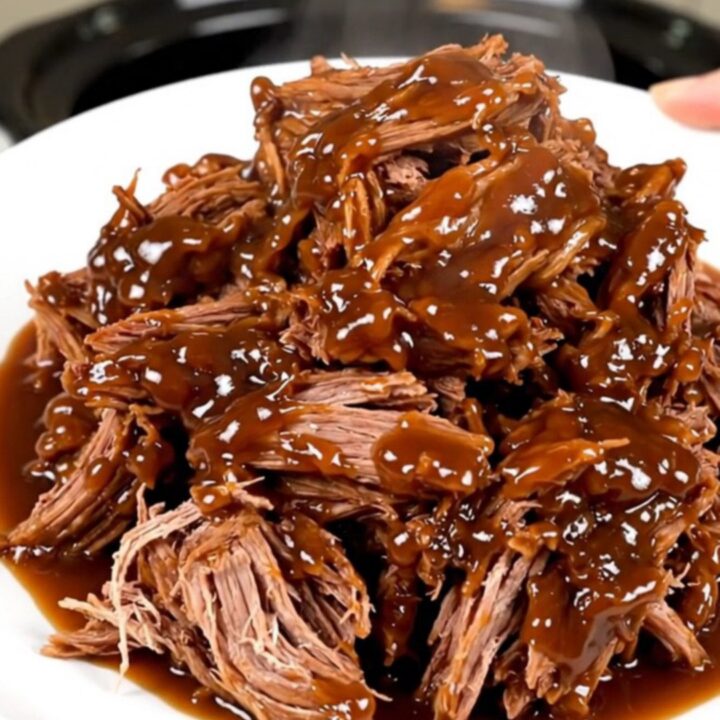 A close-up of tender, shredded apple cider pulled pork served on a white plate.