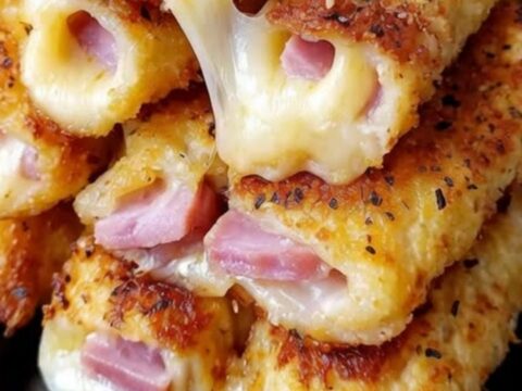 A stack of crispy, golden-brown ham and cheese mozzarella sticks on a black plate with melted cheese oozing out.