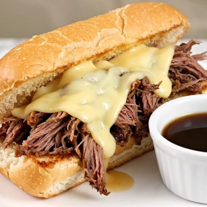 A warm, toasted hoagie roll filled with shredded beef and melted provolone cheese on a white plate.