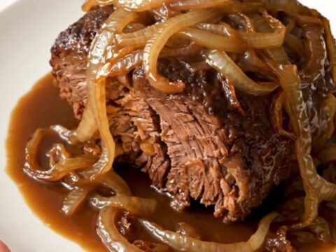 A close-up of a tender, slow-cooked beef roast served on a white plate with caramelized onions.