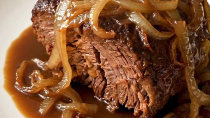 A close-up of a tender, slow-cooked beef roast served on a white plate with caramelized onions.